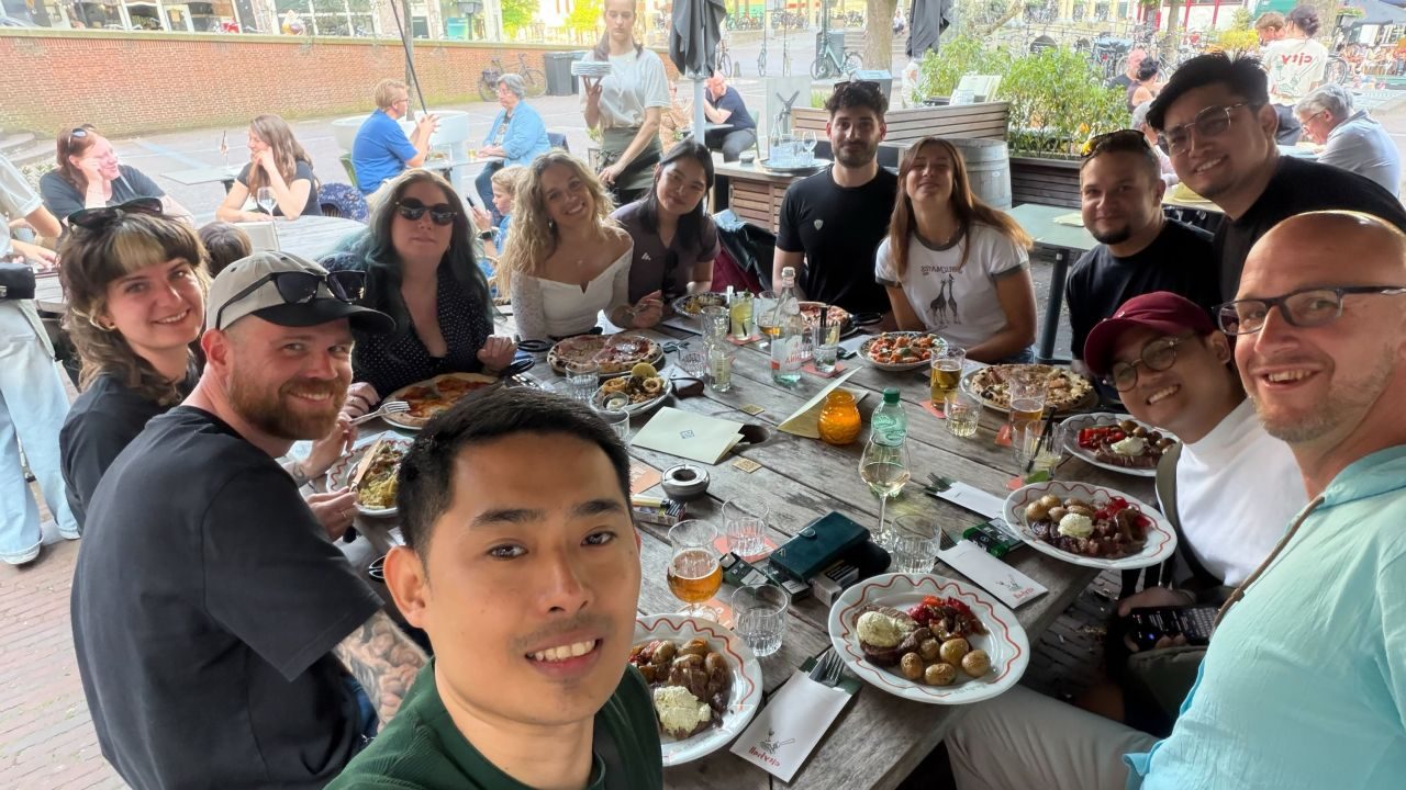 Colleagues smiling around a long outdoor table with food and drinks.