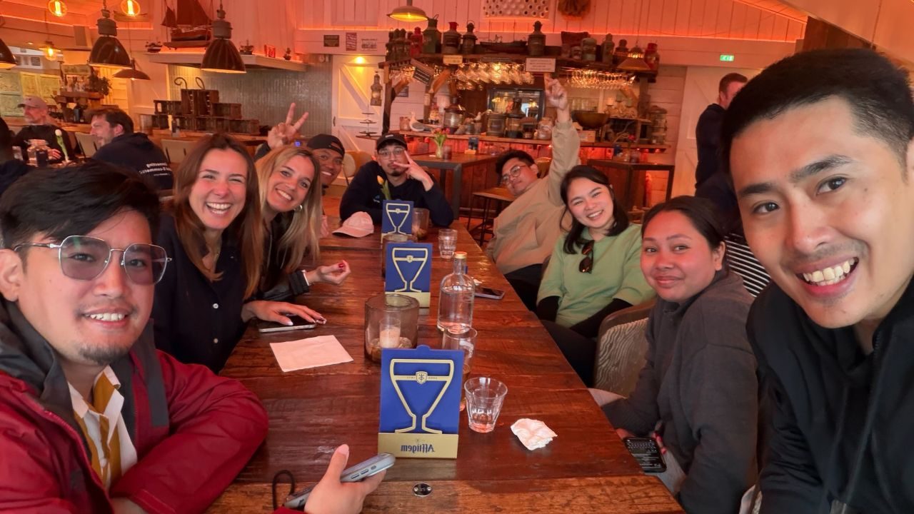 Colleagues around a wooden table in a restaurant, some making peace signs.