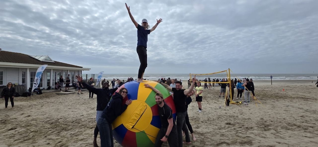 Colleagues posing around a giant colourful beach ball on the beach.
